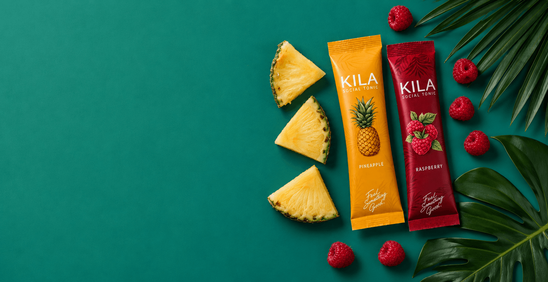 KILA Pineapple and Raspberry sticks with fresh fruit and tropical leaves on a teal backdrop